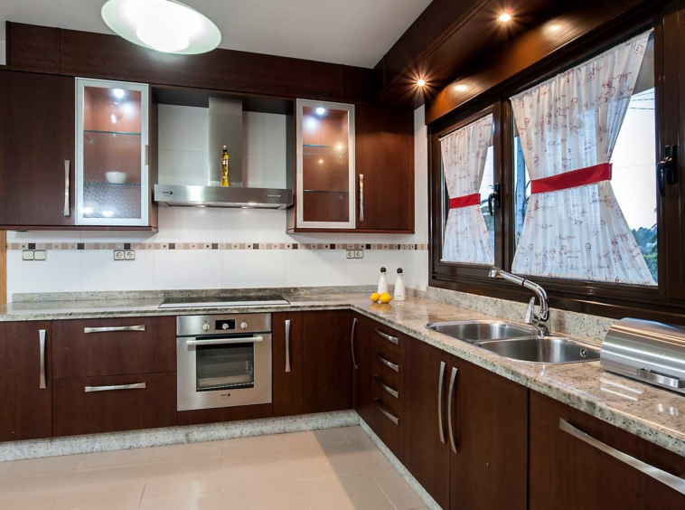 Cocina espaciosa con electrodomésticos en acero inoxidable y fregadero bajo ventana_ unifamiliar coirós