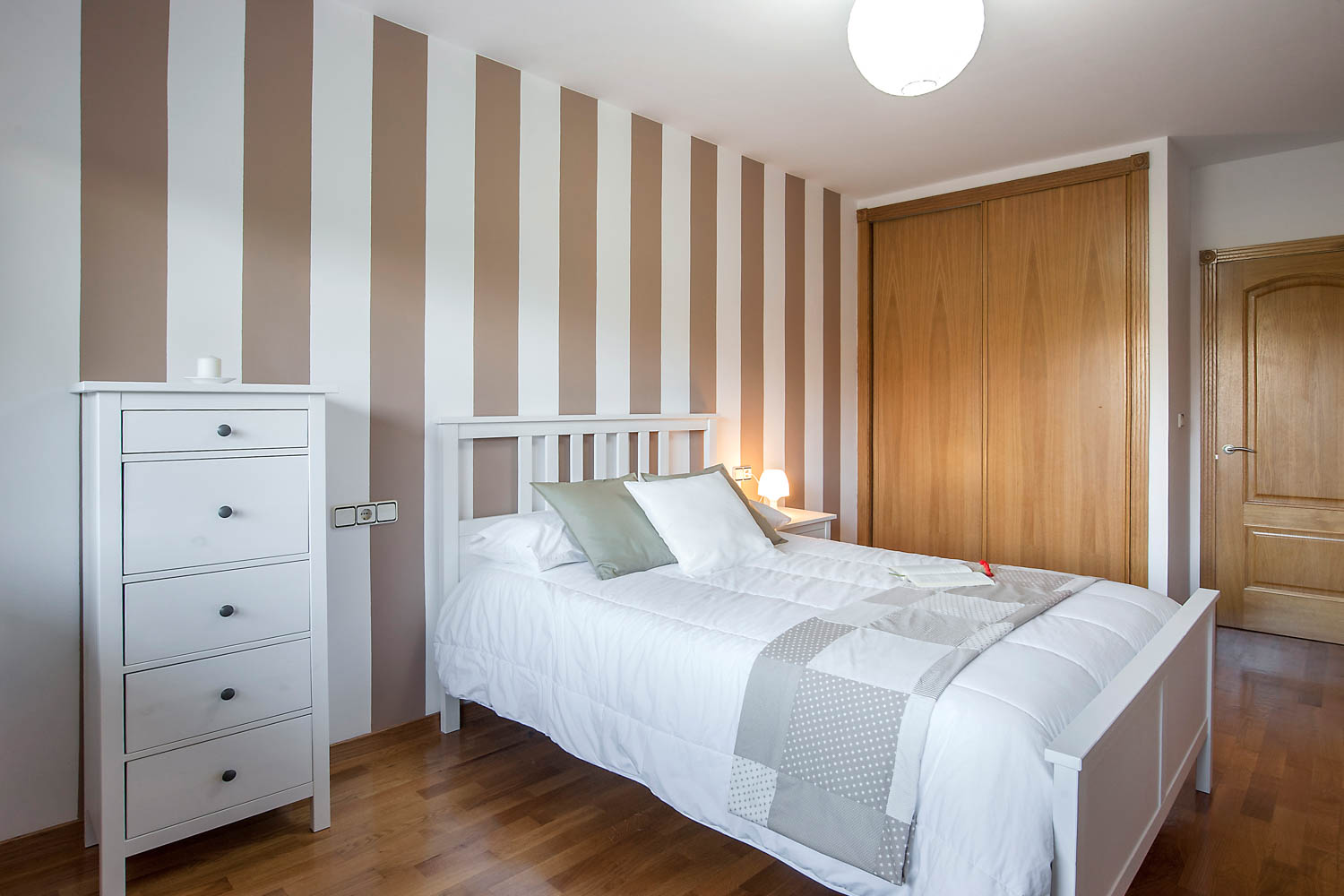 Dormitorio pared a rayas en unifamiliar Coirós_ armario empotrado de madera y cama blanca