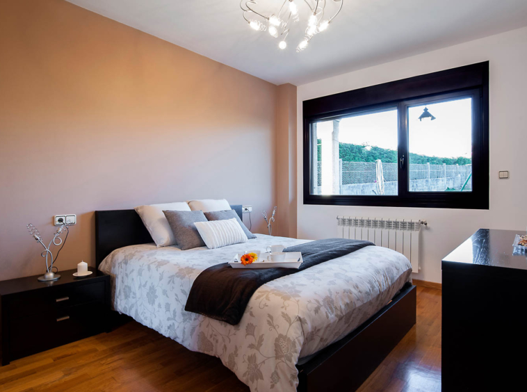 Dormitorio principal vivienda unifamiliar Coirós_ Textiles de cama en tonos beige con motivos de flores y muebles oscuros_ ventana
