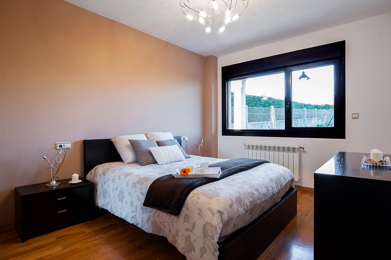 Dormitorio principal vivienda unifamiliar Coirós_ Textiles de cama en tonos beige con motivos de flores y muebles oscuros_ ventana