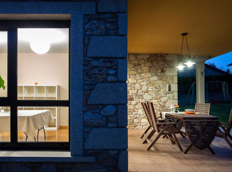 Fotografía nocturna vivienda unifamiliar de piedra en Coirós_ Porche con comedor y salón