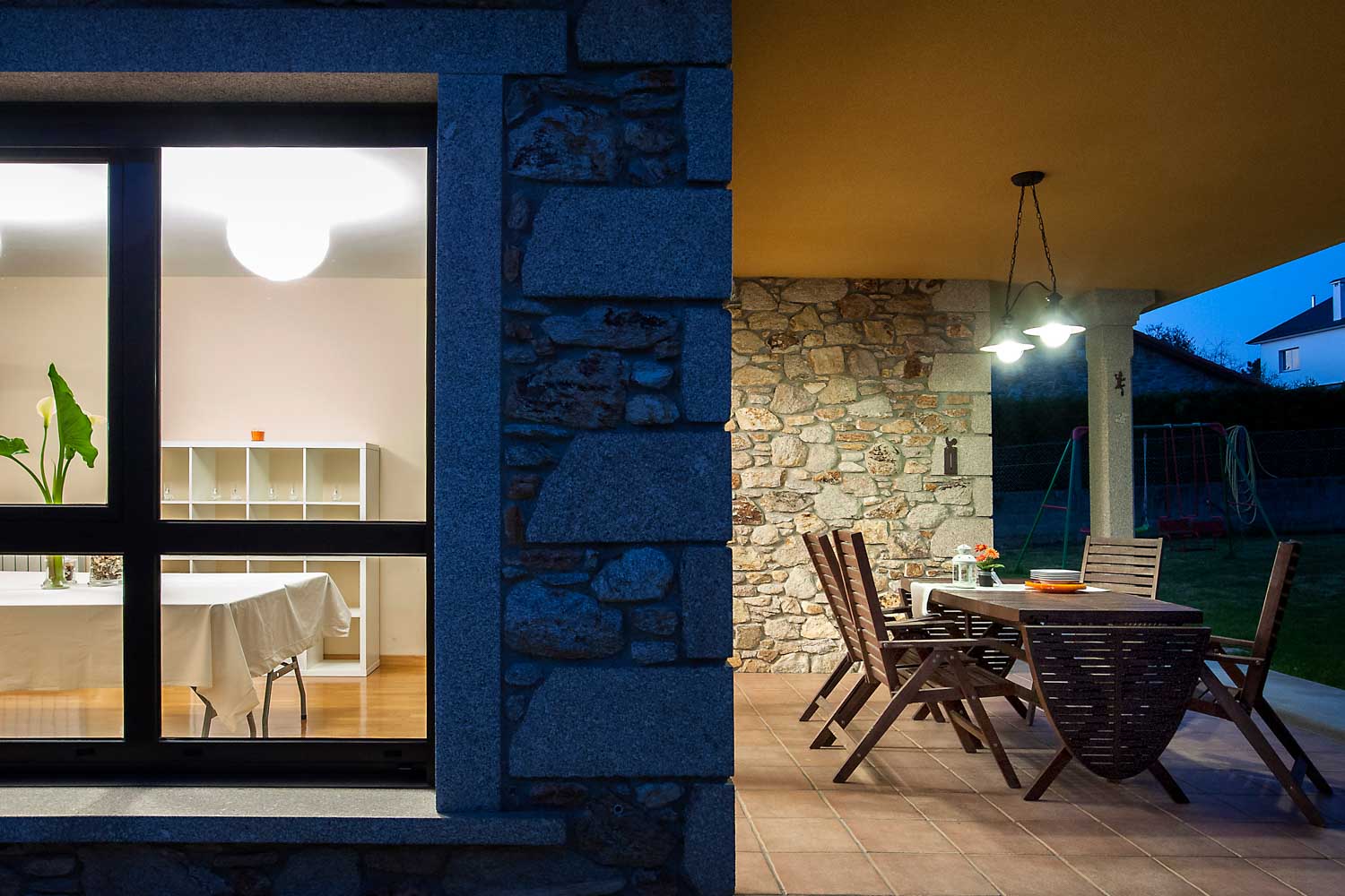 Fotografía nocturna vivienda unifamiliar de piedra en Coirós_ Porche con comedor y salón