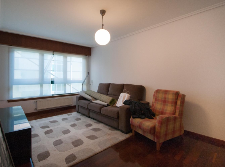 Salón previo al home staging_ sofá gris y butaca de cuadros con alfombra geométrica