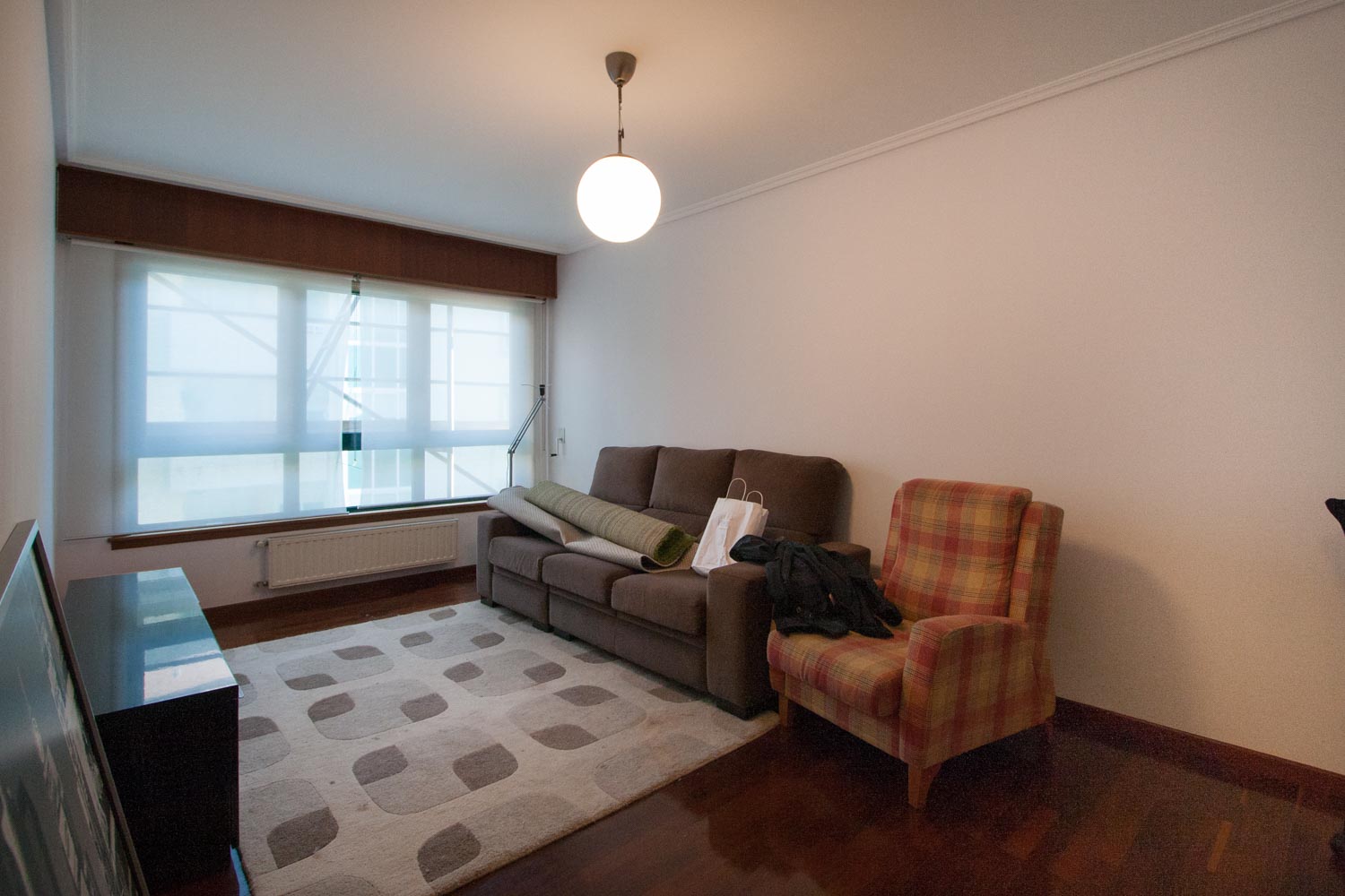 Salón previo al home staging_ sofá gris y butaca de cuadros con alfombra geométrica