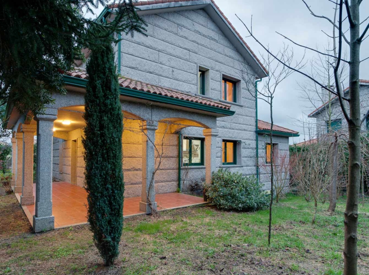Fachada de granito con porche y cubierta de teja curva_ carpinterías verdes_ vivienda unifamiliar en Bergondo