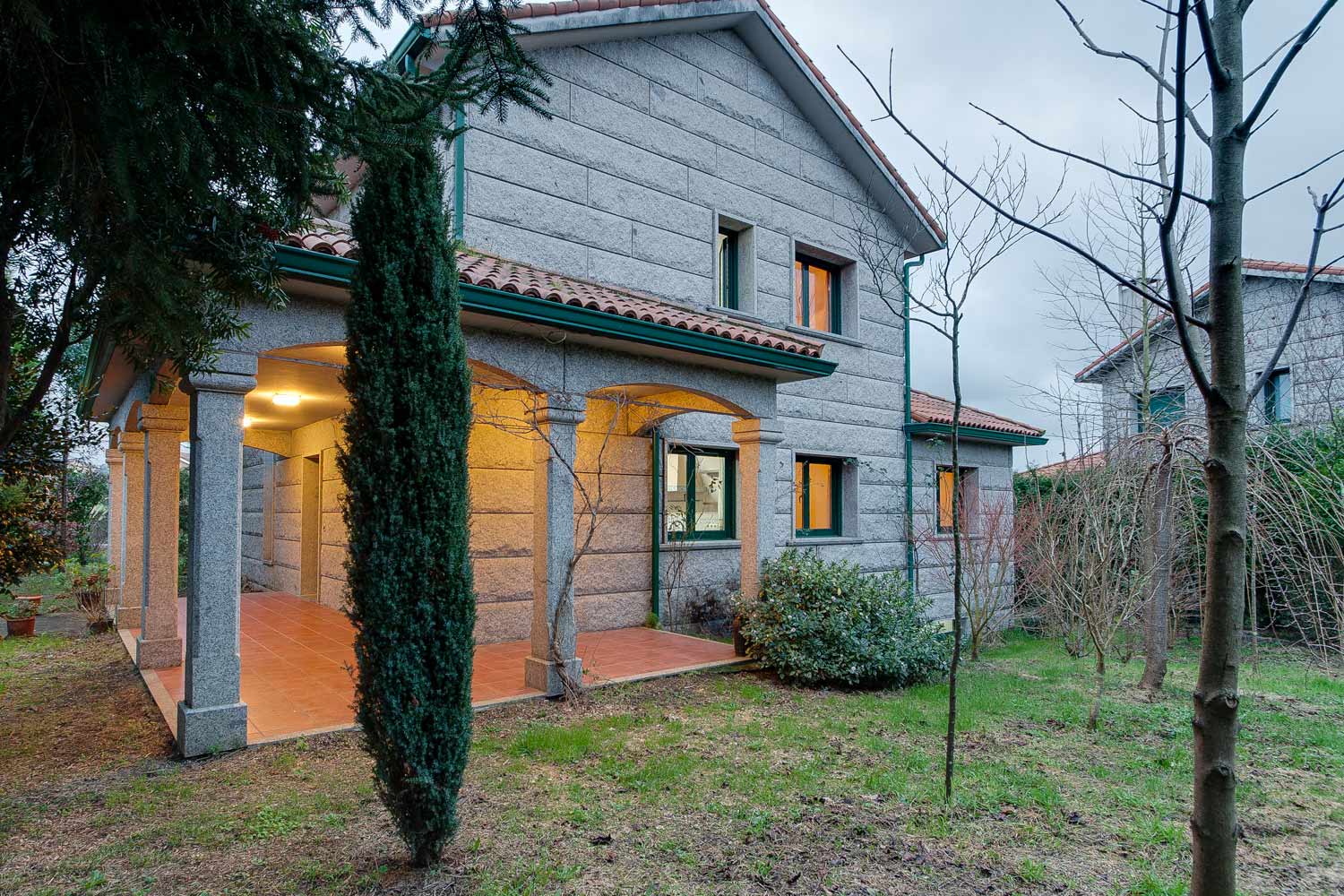 Fachada de granito con porche y cubierta de teja curva_ carpinterías verdes_ vivienda unifamiliar en Bergondo