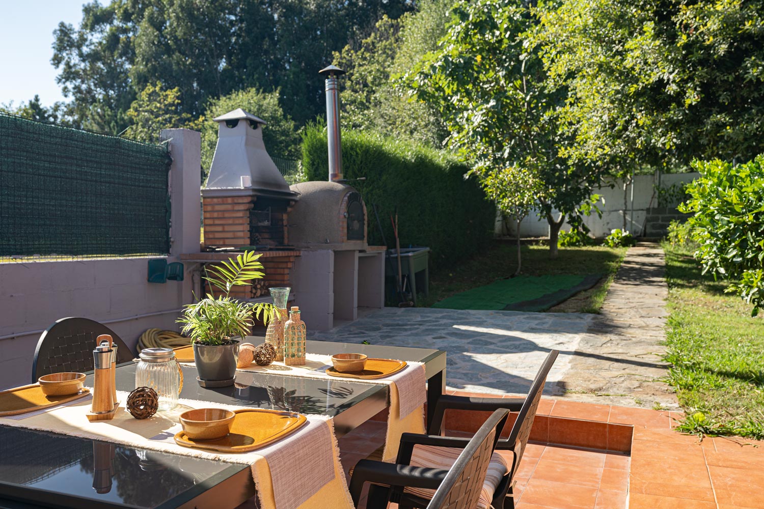 Terraza con mesa y sillas, junto a zona de barbacoa en el jardín