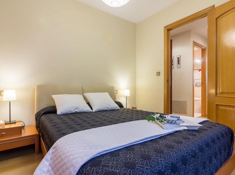 Dormitorio principal con Home Staging_ puerta abierta hacia pasillo y cama de matrimonio con colcha gris y cojines blancos_ bandeja de desayuno sobre la cama