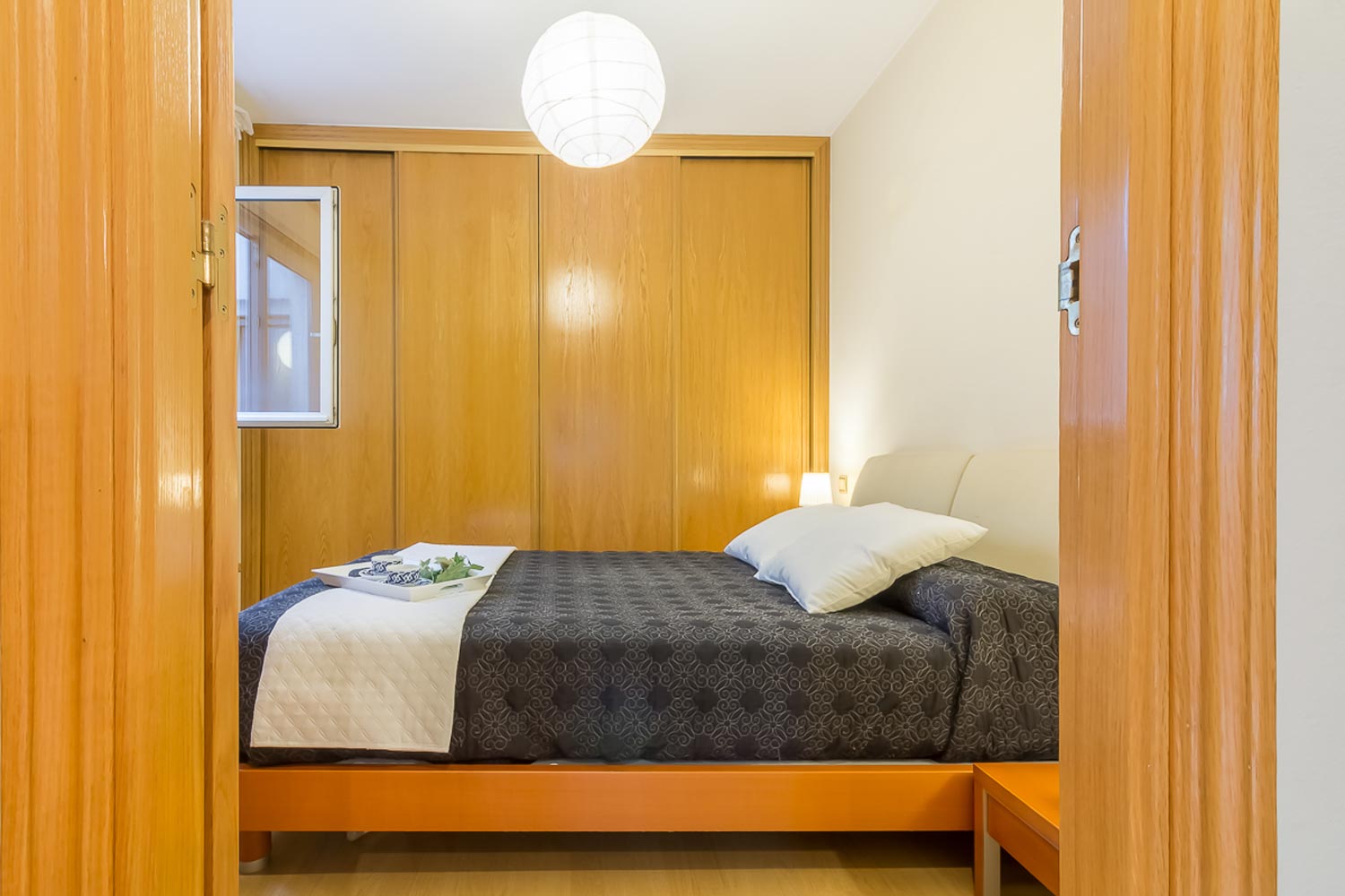 Dormitorio principal con Home Staging_ armario empotrado pared del fondo y cama de matrimonio con colcha gris y cojines blancos_ bandeja de desayuno sobre la cama