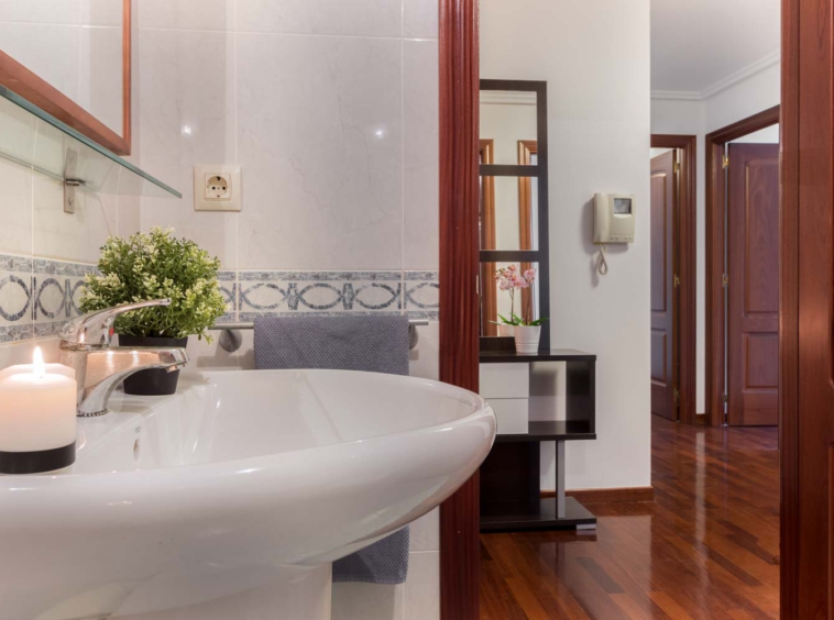 Cuarto de baño clásico blanco con cenefa azul y lavabo de pie_ puerta abierta hacia recibidor con suelos de parqué brillante_ Home Staging