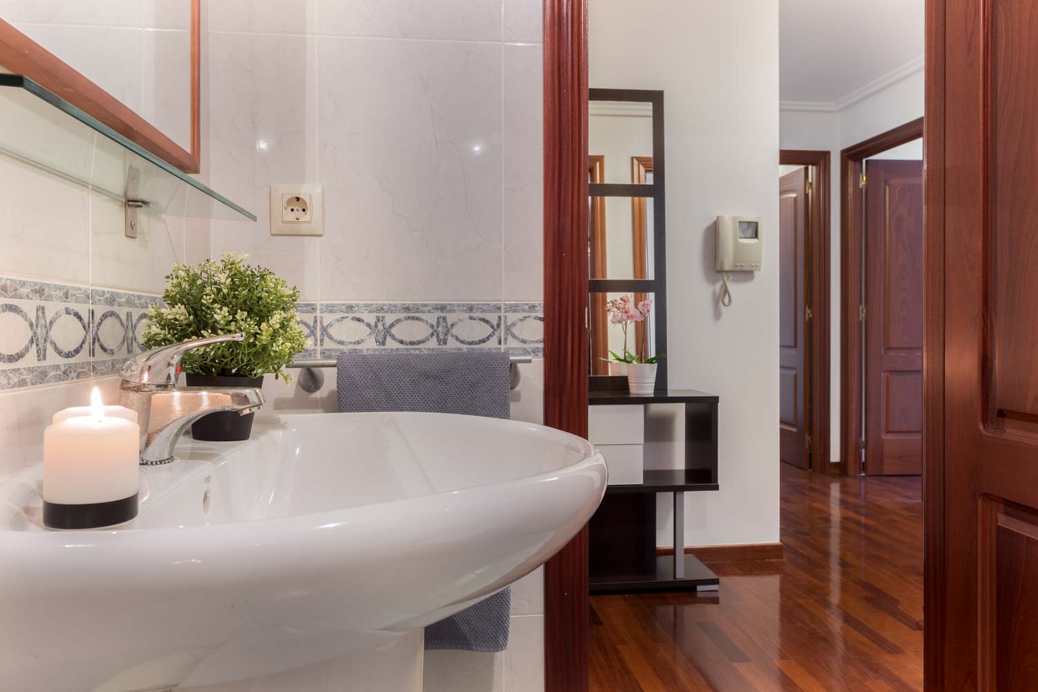 Cuarto de baño clásico blanco con cenefa azul y lavabo de pie_ puerta abierta hacia recibidor con suelos de parqué brillante_ Home Staging