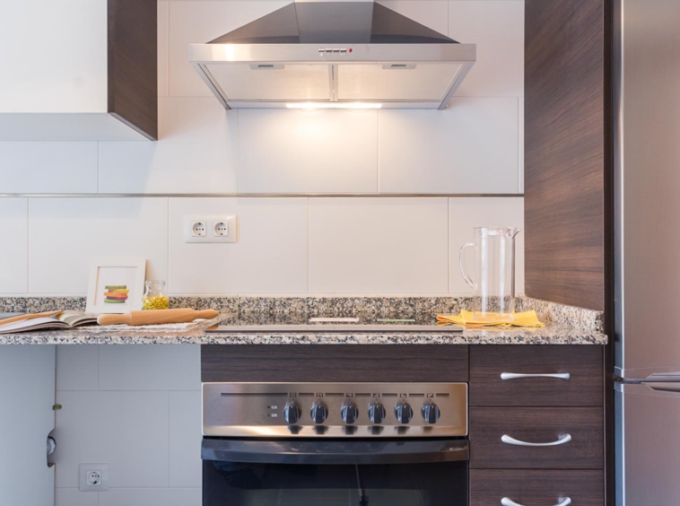 Frontal de cocina con electrodomésticos en acero inoxidable y encimera de granito gris y marrón_ rodillo y libro de recetas