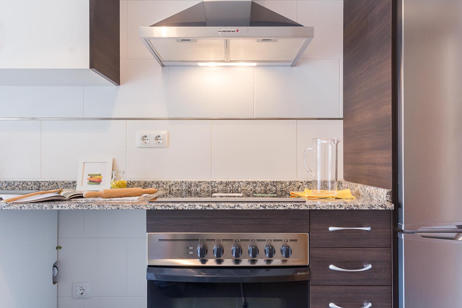 Frontal de cocina con electrodomésticos en acero inoxidable y encimera de granito gris y marrón_ rodillo y libro de recetas