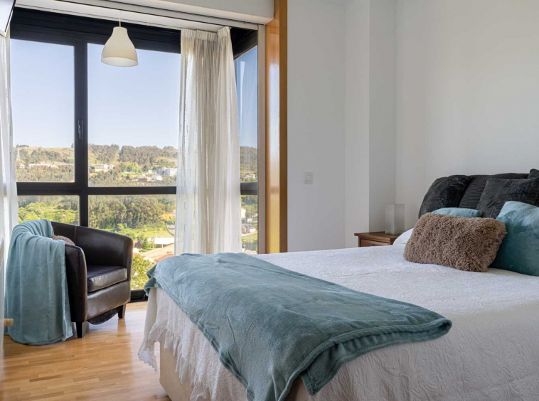 Dormitorio doble con textiles neutros y azules_ gran ventanal con vistas al paisaje y butaca junto a él