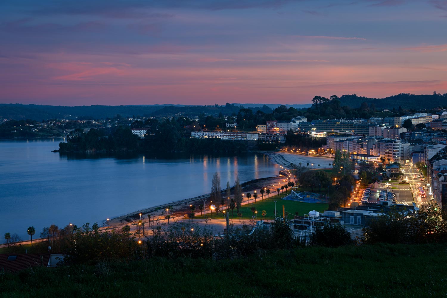 Finca en venta en Sada, A Coruña con vistas al atardecer sobre el mar, destacando la iluminación urbana y costera.