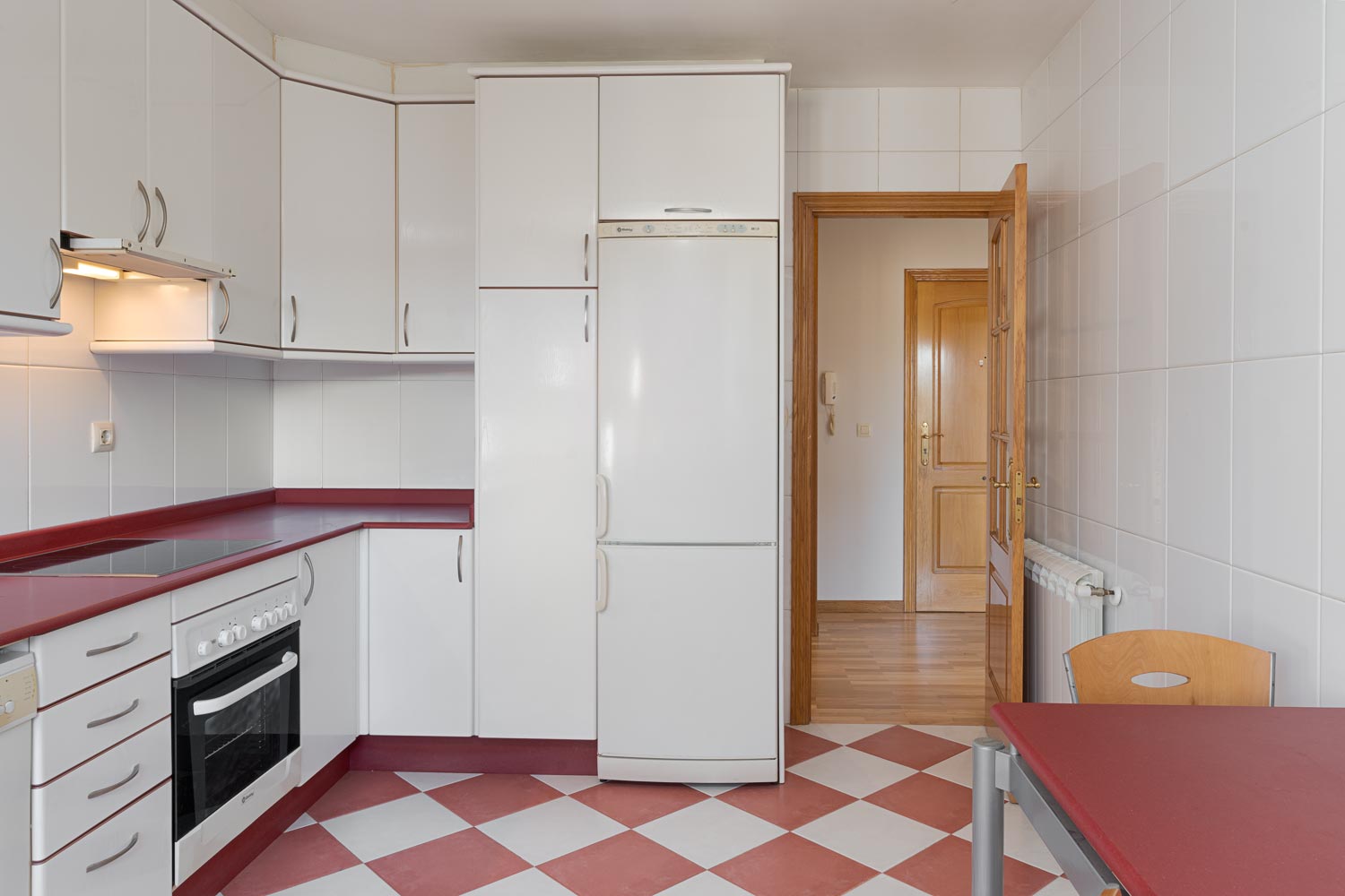 Cocina clásica con mesa roja y electrodomésticos integrados, iluminada y acogedora, en piso en Sada, listo para entrar a vivir.
