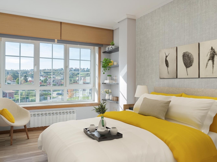 Un dormitorio moderno con grandes ventanas y vistas al exterior, con cama con ropa blanca y colcha amarilla, cuadros abstractos en la pared, y un sillón junto a la ventana, preparado con home staging