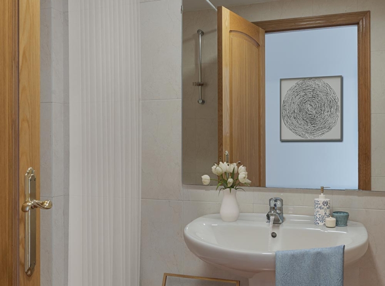 Baño con un lavabo de pedestal, un espejo con marco de madera, una bañera con cortina blanca y detalles decorativos como flores y una toalla de mano con patrón de chevron en un toallero de madera