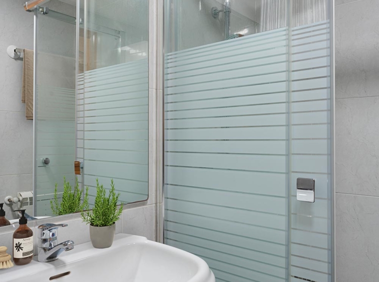 Baño contemporáneo con lavabo sobre mueble de madera oscura, accesorios de baño, una planta pequeña y una cabina de ducha con puertas de vidrio y azulejos claros.