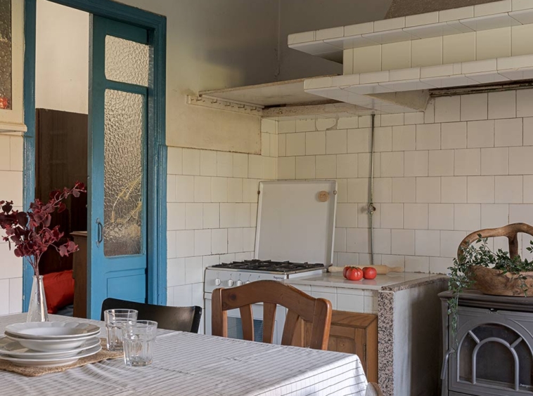 Cocina rústica con mesa de madera, sillas y una estufa antigua, ofreciendo un ambiente tradicional y acogedor en una casa de Bergondo, A Coruña