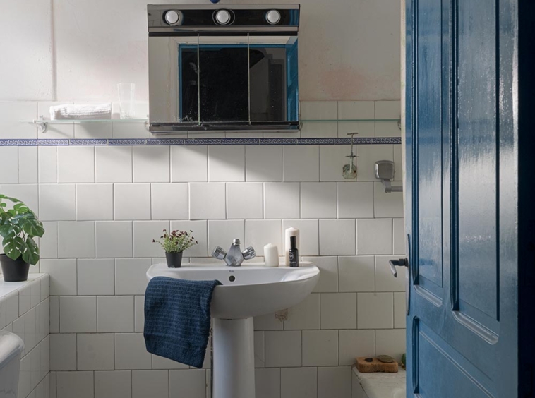 Baño sencillo con azulejos blancos, puerta azul y accesorios básicos, reflejando un estilo funcional y sin pretensiones en una casa en Bergondo, A Coruña
