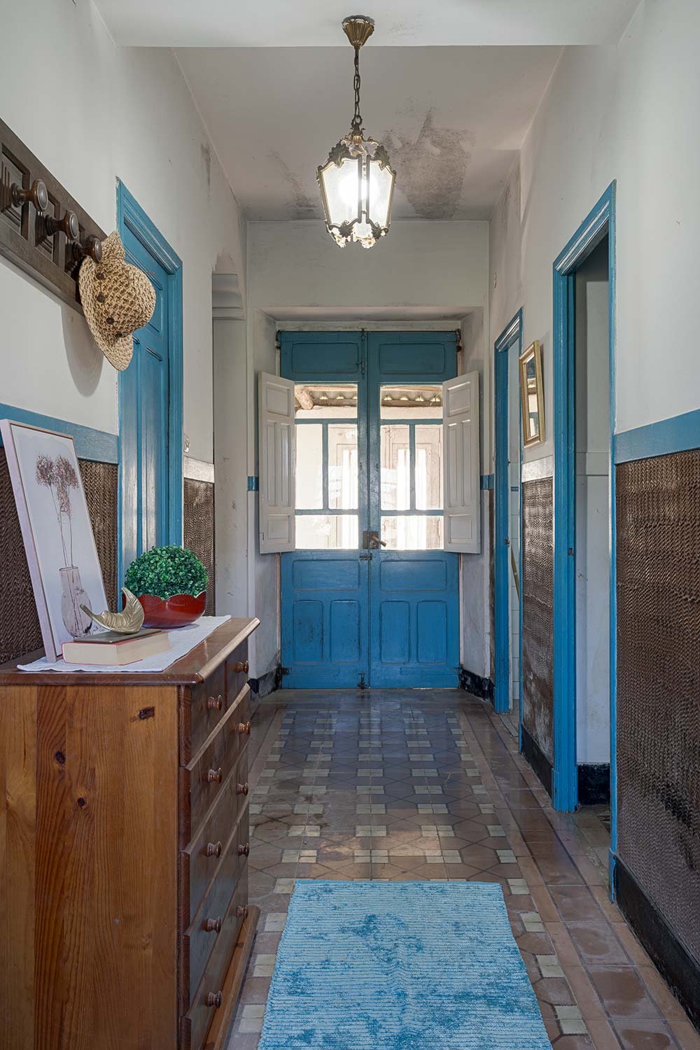 vestíbulo de entrada con puertas dobles azules, suelo de baldosas, y una lámpara antigua colgante, creando una entrada acogedora en una casa de Bergondo, A Coruña.
