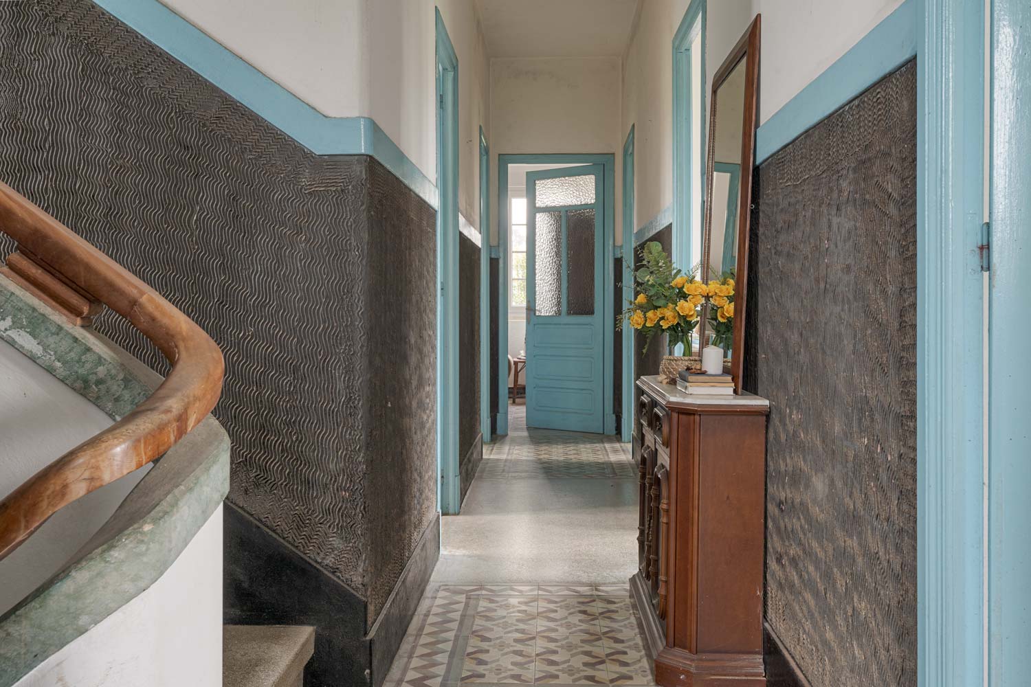 Pasillo de entrada de casa con escalera de madera, puertas azules y decoración floral, transmitiendo una sensación de bienvenida en una casa de Bergondo, A Coruña