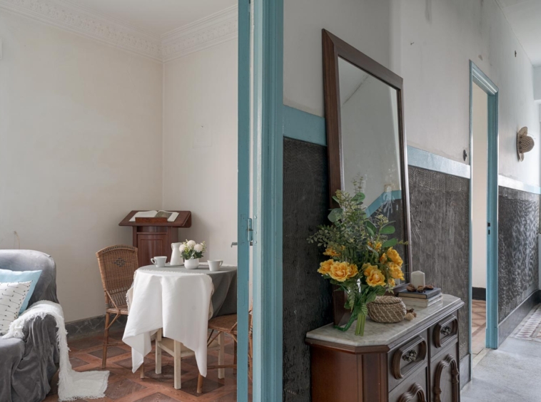 Sala de estar rústica con una pequeña mesa de comedor, sillas de mimbre, y un arreglo floral en una casa de Bergondo, A Coruña