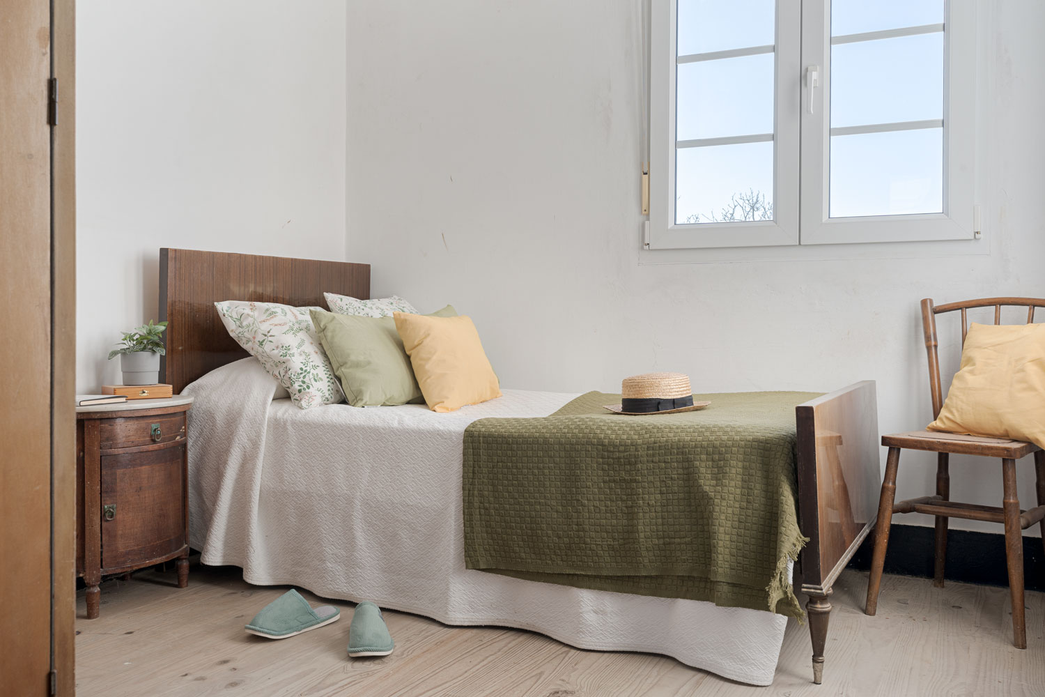 Habitación sencilla y bien iluminada con cama de madera, ropa de cama en tonos suaves y un sombrero de paja sobre la colcha, en una casa de Bergondo, A Coruña