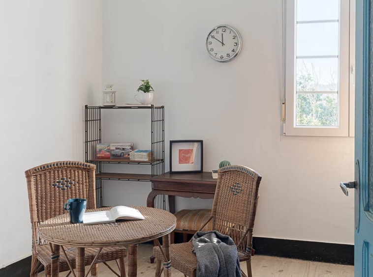 Espacio de trabajo en casa con una mesa redonda de ratán, sillas a juego y una estantería con libros, bajo la luz de una ventana en una casa de Bergondo, A Coruña.
