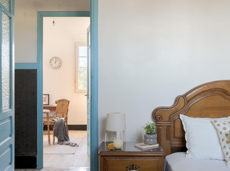Vista parcial de una habitación con una cama de madera clásica y una mesa de noche con una lámpara moderna, y una mirada al espacio de trabajo contiguo, en una casa de Bergondo, A Coruña