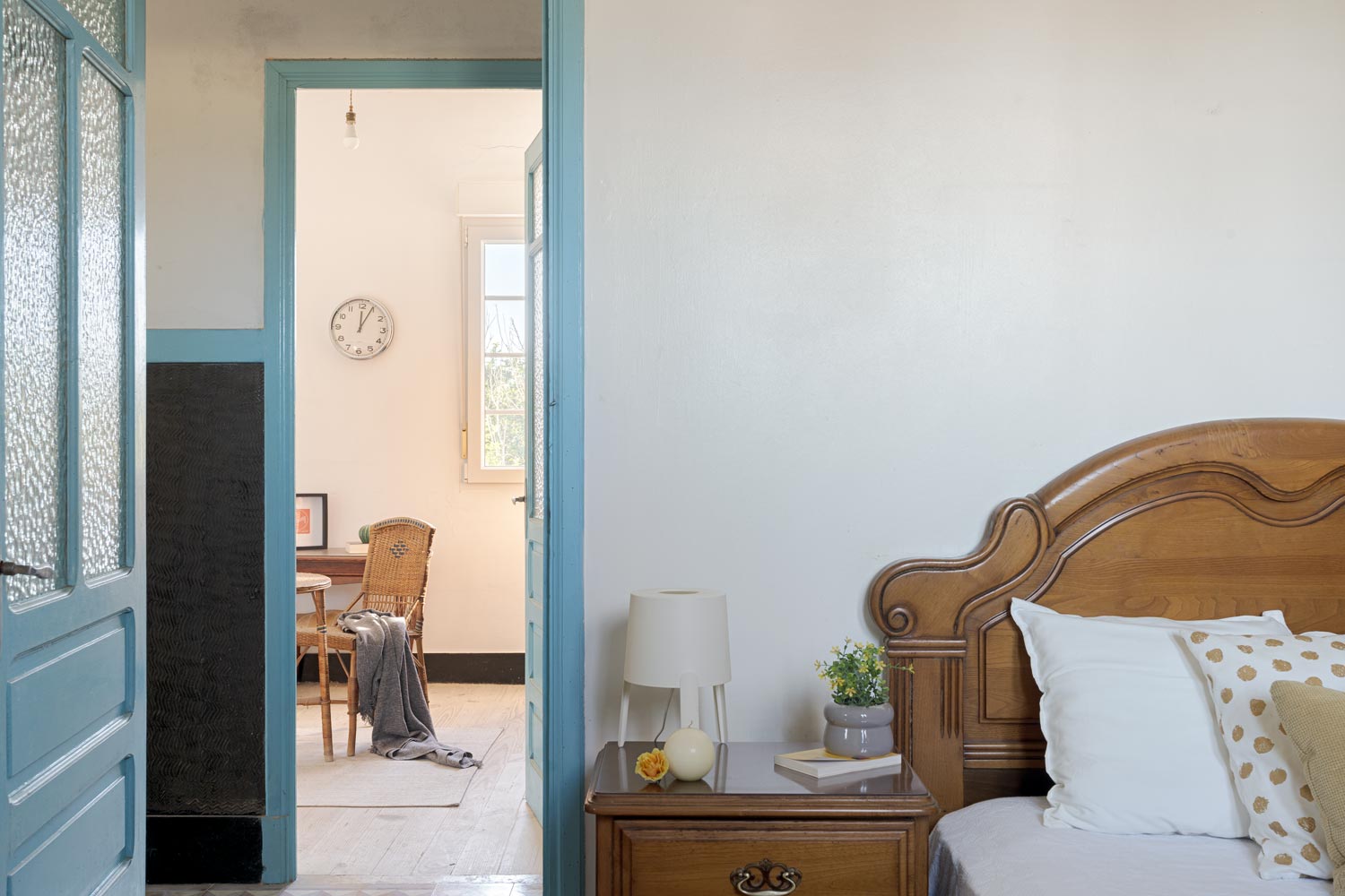Vista parcial de una habitación con una cama de madera clásica y una mesa de noche con una lámpara moderna, y una mirada al espacio de trabajo contiguo, en una casa de Bergondo, A Coruña