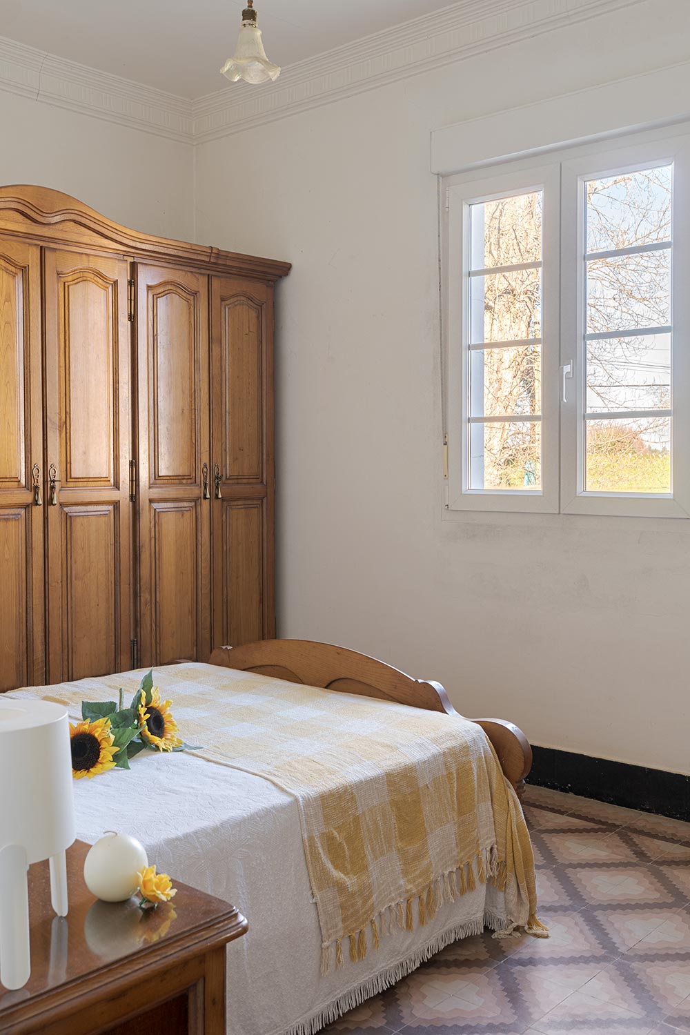 Dormitorio luminoso con cama de madera, armario clásico y detalles florales, destacando una atmósfera tranquila y tradicional en una casa de Bergondo, A Coruña