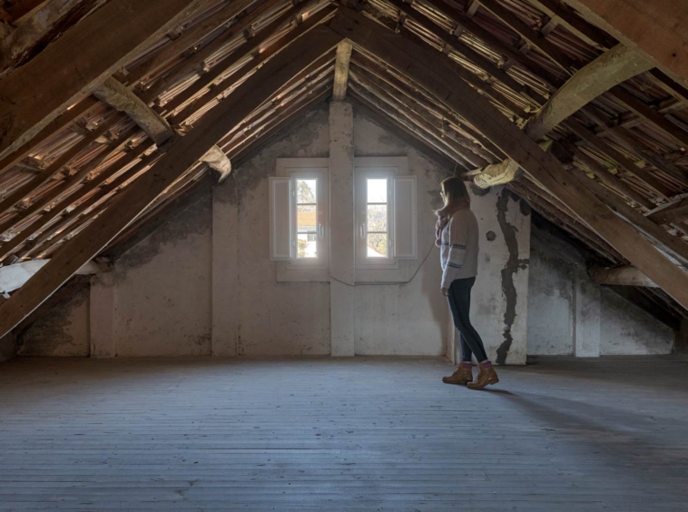 Ático espacioso sin amueblar con estructura de madera visible, ventana pequeña y suelo de tablones de madera, en una casa de Bergondo, A Coruña