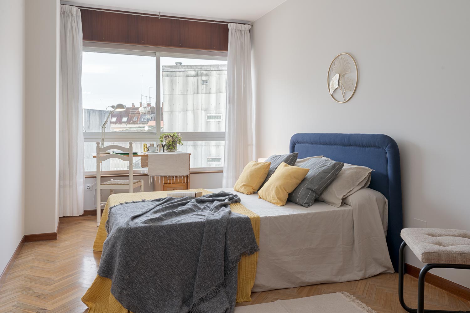 Dormitorio principal en un piso en Sada, A Coruña, decorado con técnicas de home staging, destacando una cama con cabecero azul y cojines amarillos y grises