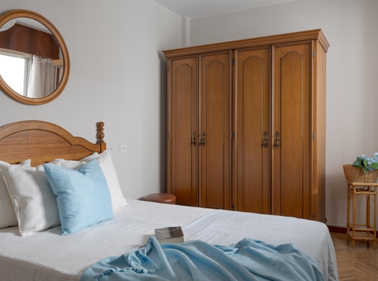 Dormitorio sereno con decoración de home staging, mostrando una cama con cabecero de madera, armario amplio y espejo redondo en un piso en venta en Sada, A Coruña