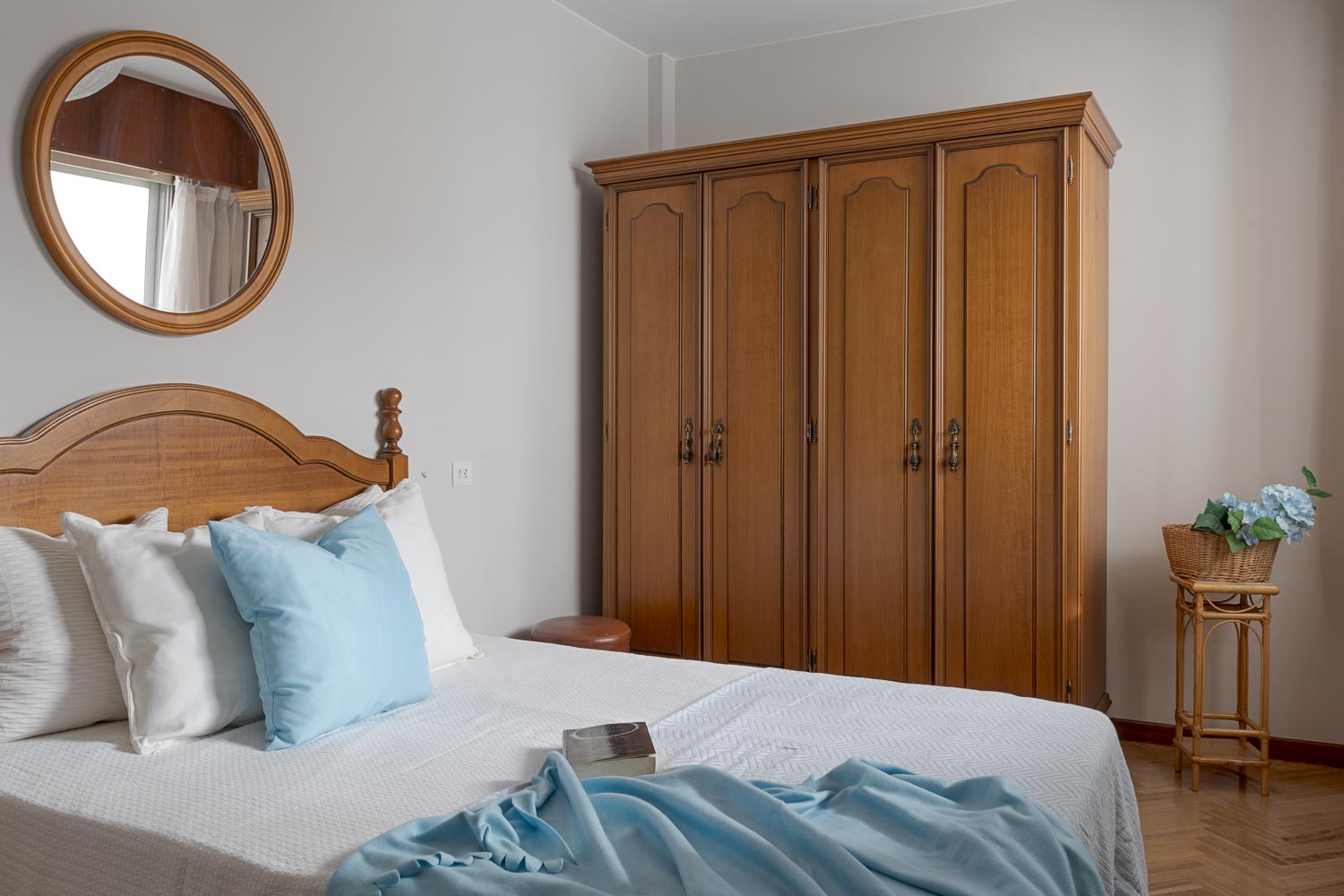 Dormitorio sereno con decoración de home staging, mostrando una cama con cabecero de madera, armario amplio y espejo redondo en un piso en venta en Sada, A Coruña