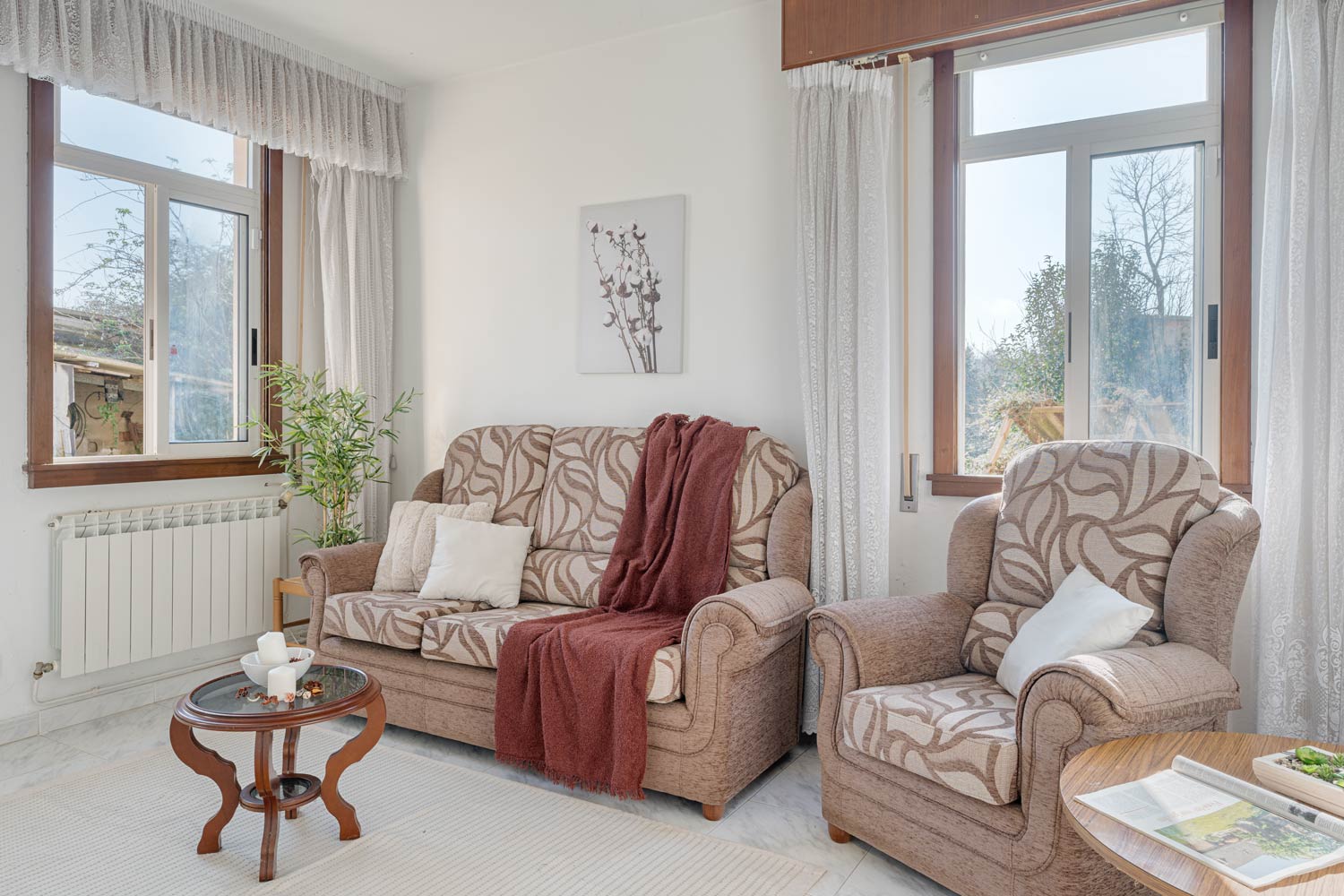 Sala de estar luminosa con sofá y sillones estampados y ventana con vistas al jardín.