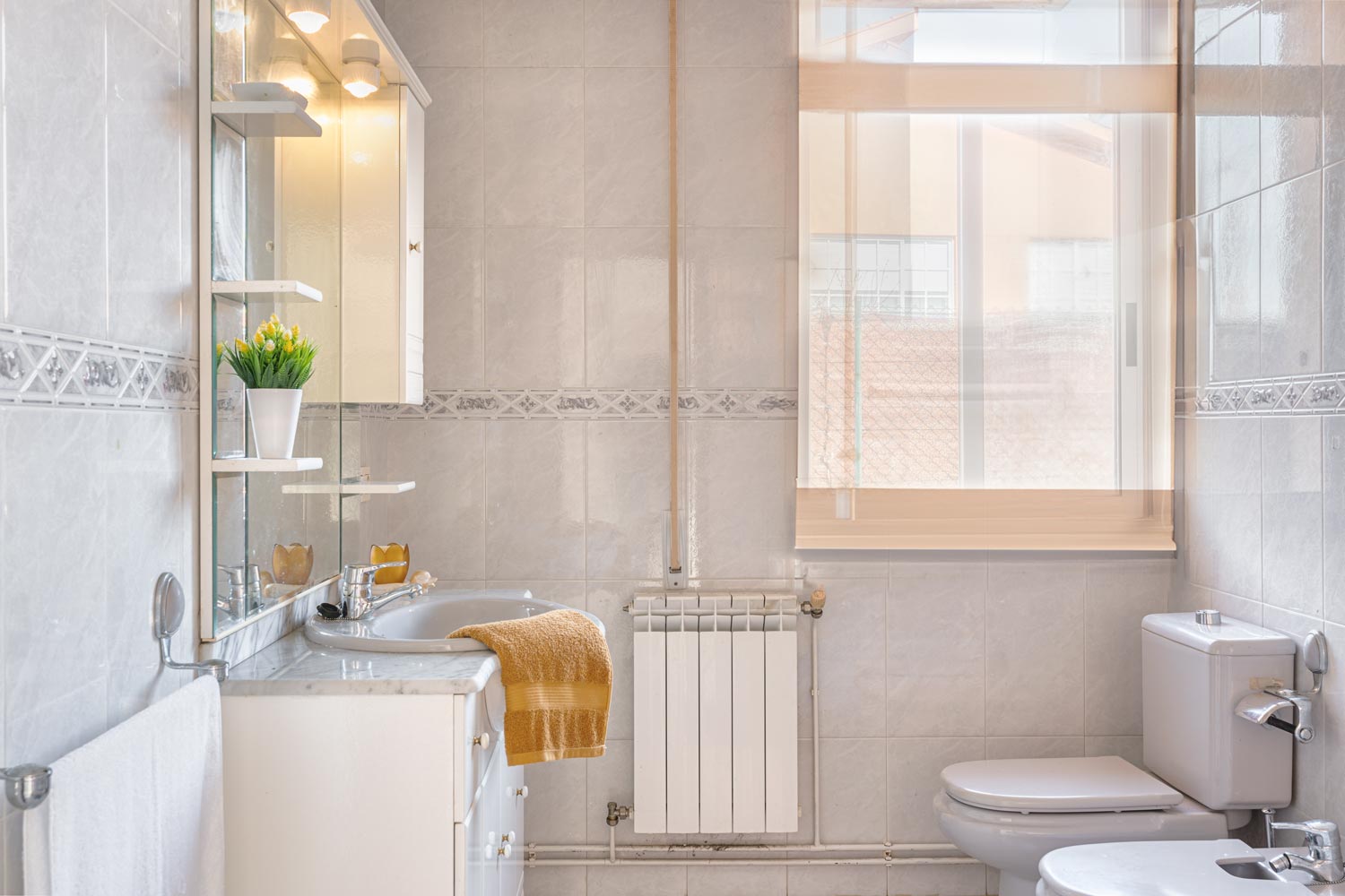 Baño luminoso con azulejos en tonos beige, espejo amplio y ventana que ofrece luz natural.