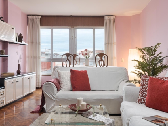 Sala de estar con paredes rosas, sofás blancos con cojines rojos, y mesa de comedor con vista a la ventana