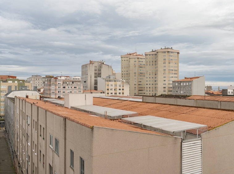 Vista urbana de A Coruña con edificios residenciales y techos de tejas bajo un cielo nublado.