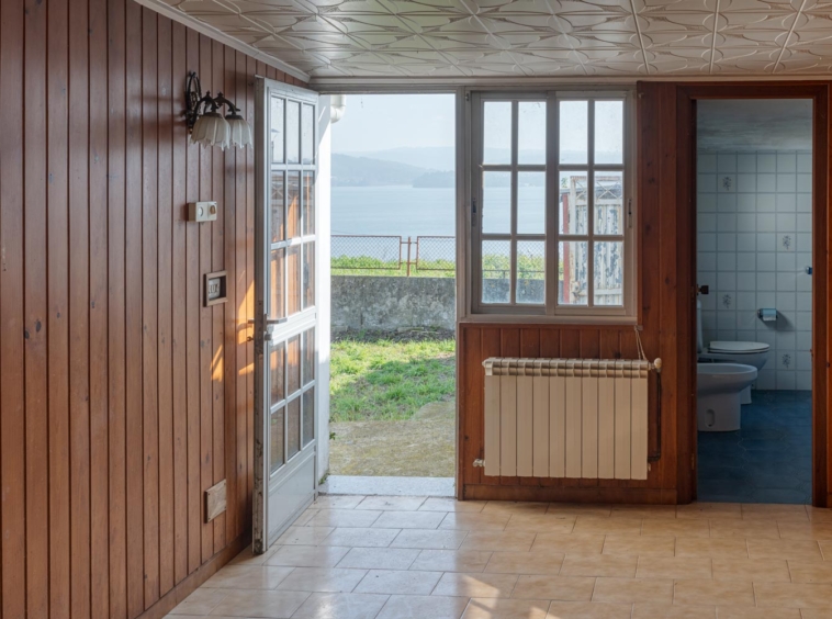 Salón y baño con puerta abierta al jardín donde se aprecian las vistas al mar