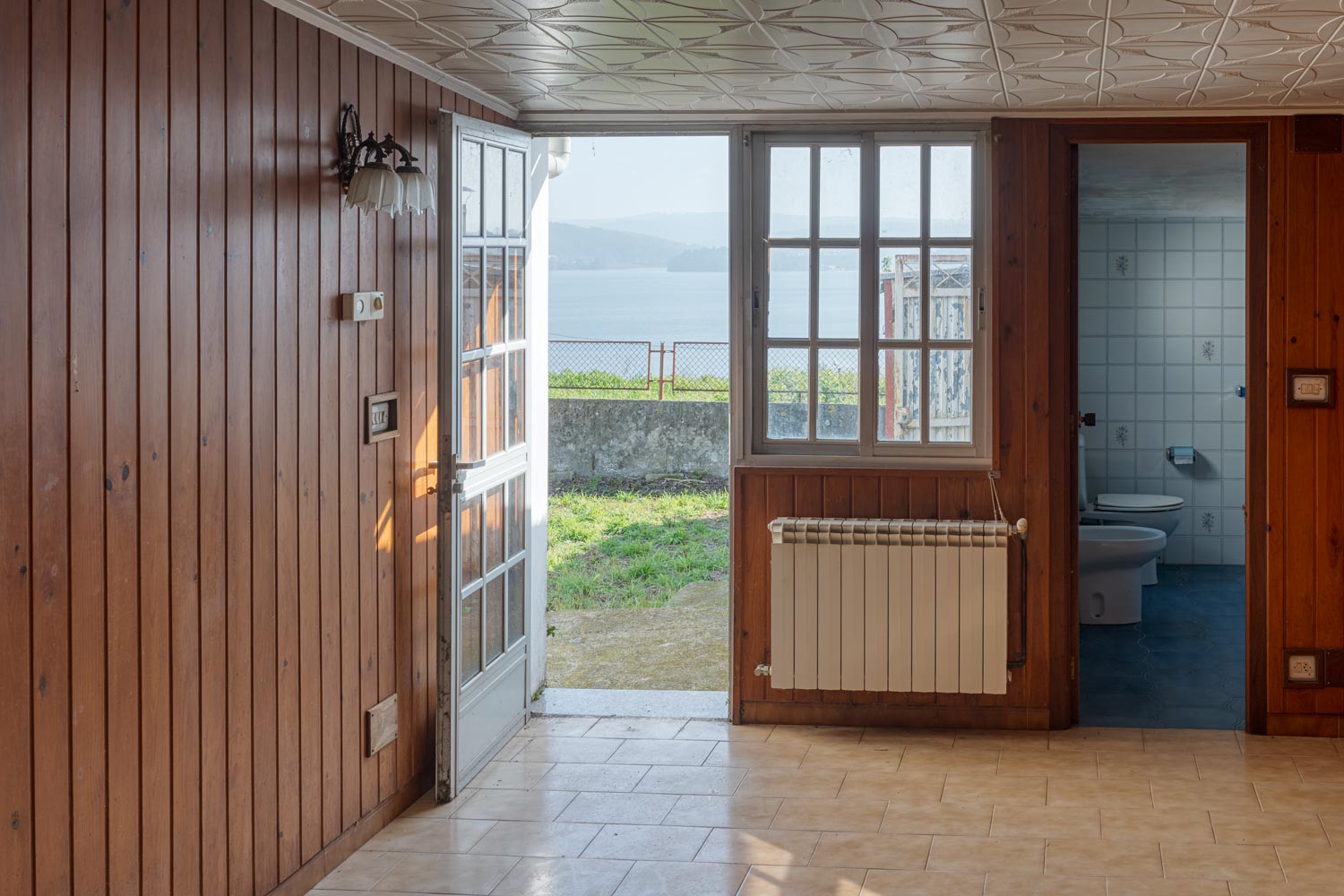 Salón y baño con puerta abierta al jardín donde se aprecian las vistas al mar