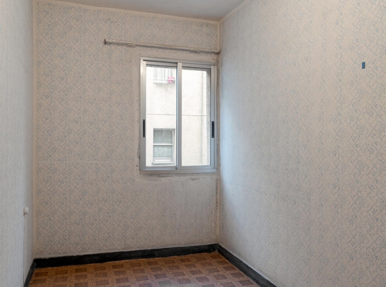 Habitación vacía con paredes de papel tapiz de patrones florales y ventana con vistas a edificio vecino en A Coruña