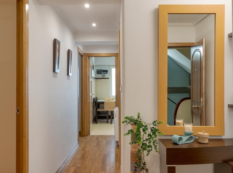 Amplio pasillo con un gran espejo biselado y suelo de madera de roble en un piso en venta en A Coruña. El pasillo conduce a la sala de estar y a los dormitorios.
