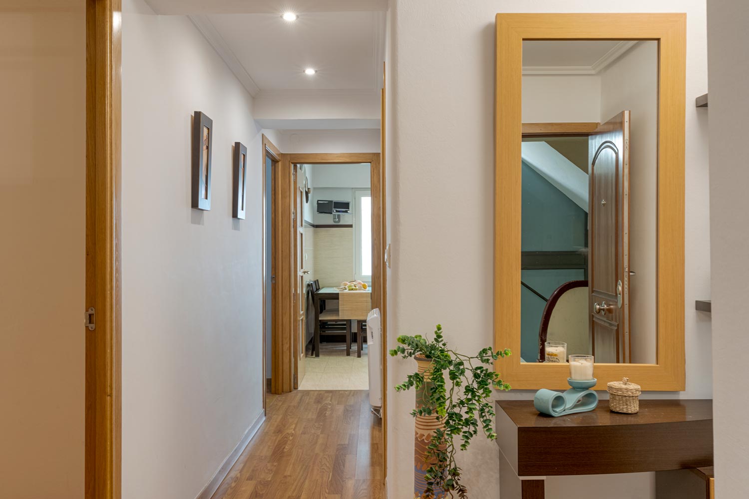 Amplio pasillo con un gran espejo biselado y suelo de madera de roble en un piso en venta en A Coruña. El pasillo conduce a la sala de estar y a los dormitorios.