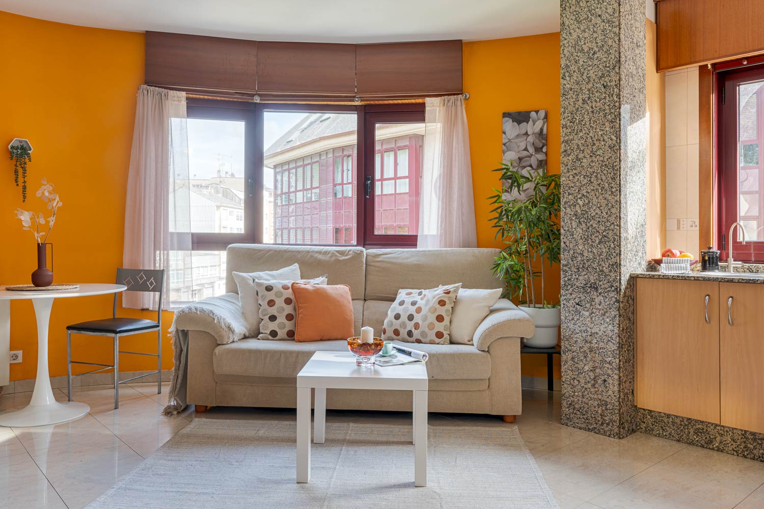 Sala de estar luminosa con un sofá en forma de L de color beige, una mesa de centro rectangular de madera con adornos y dos sillas tapizadas de color crema