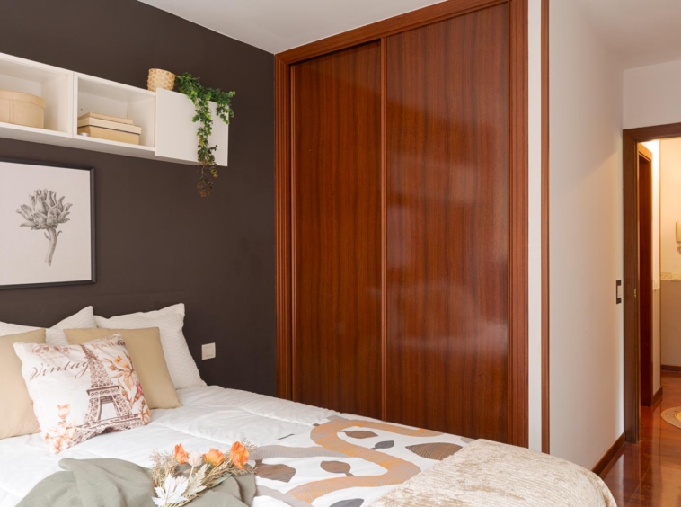 Dormitorio con armario empotrado en tono marrón chocolate y cama en tonos claros con 6 cojines a juego.