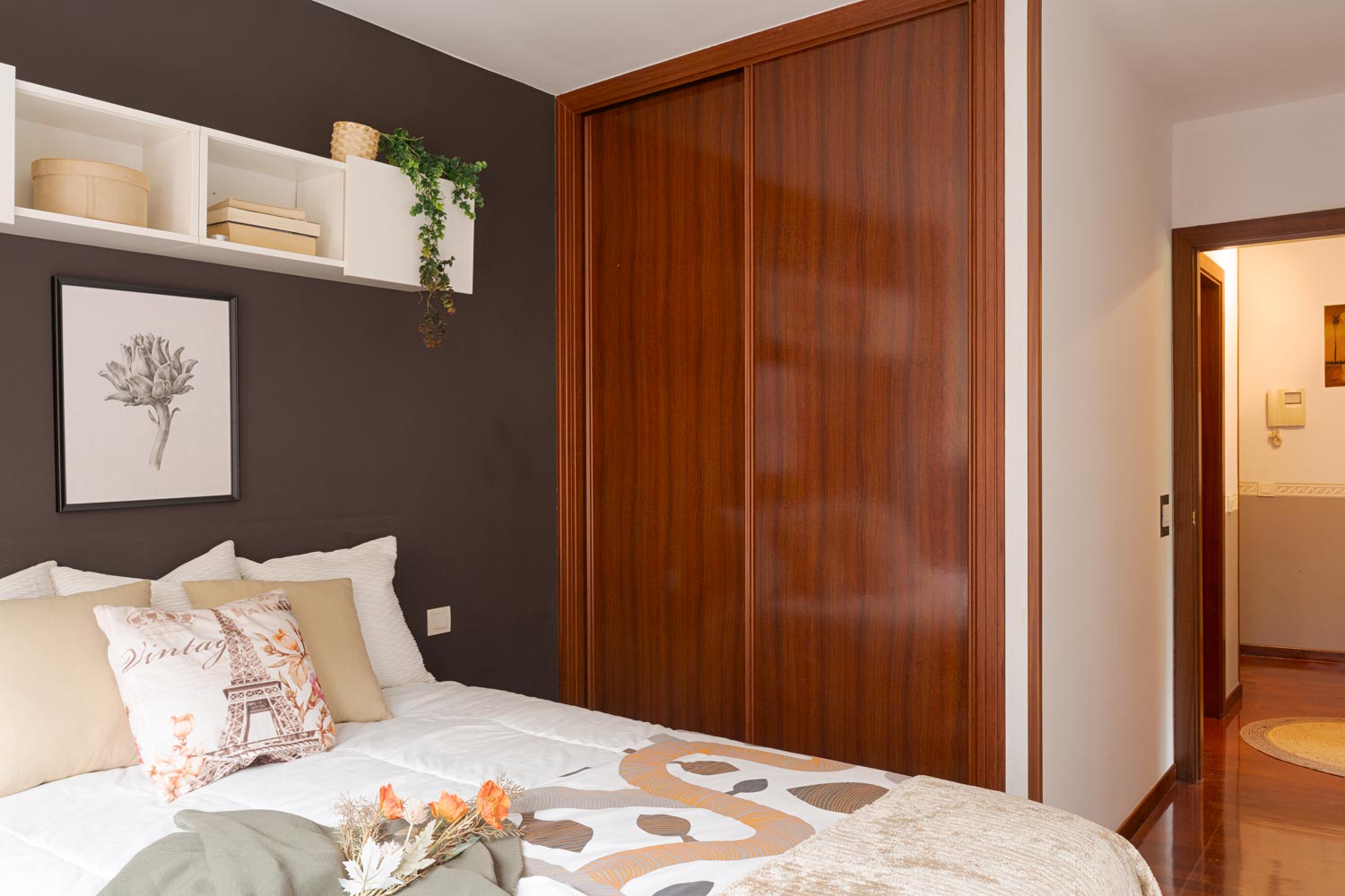 Dormitorio con armario empotrado en tono marrón chocolate y cama en tonos claros con 6 cojines a juego.